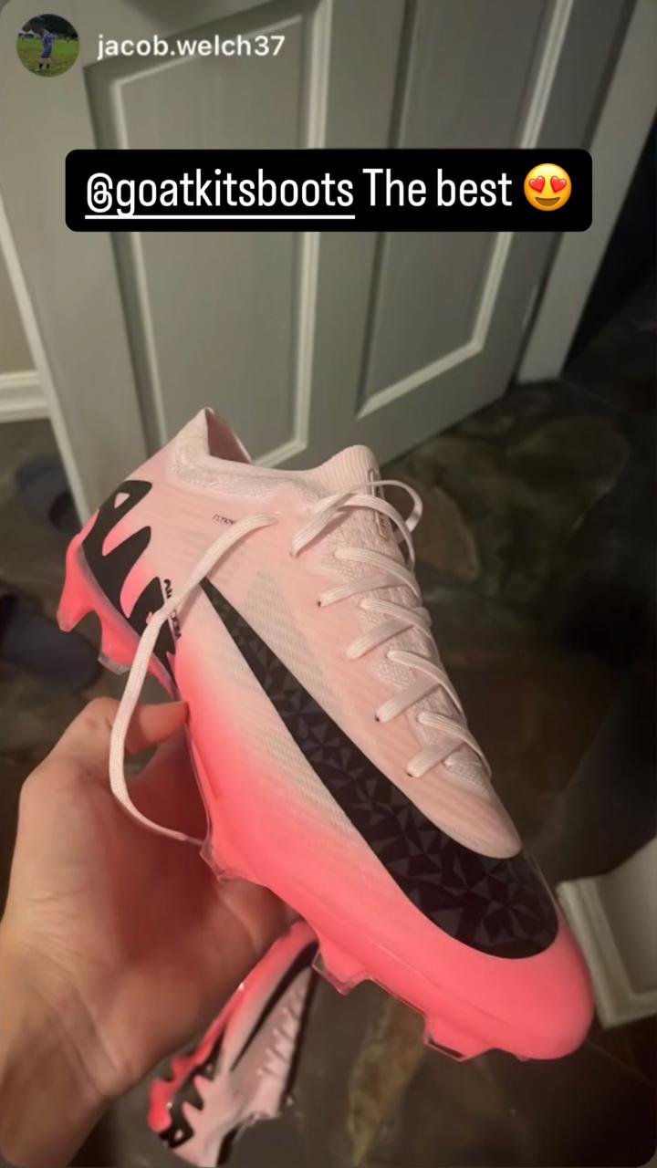 Pink Nike football boots with black accents held by a customer, tagged with @goatkitsboots and 'The best' compliment, showcasing premium sports footwear.