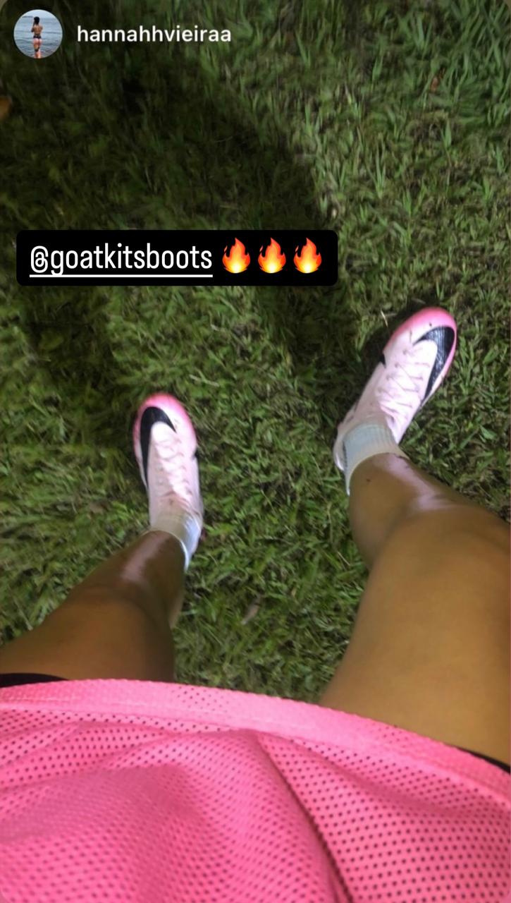 Customer wearing pink Nike football boots from GoatKits Boots on a grassy field, tagged with @goatkitsboots and fire emojis, showcasing stylish sportswear in action.